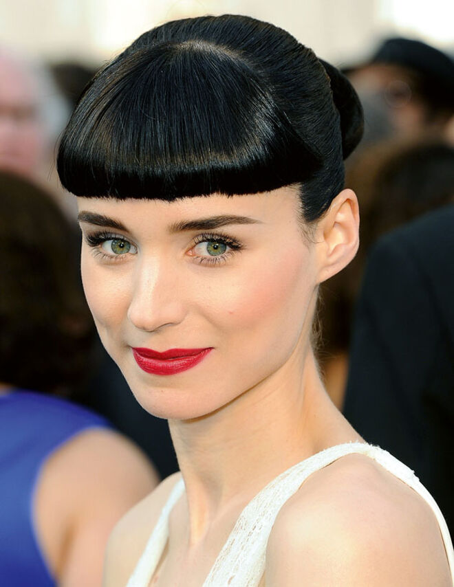 A atriz usa uma franja curta, a meio da testa e com muito volume.