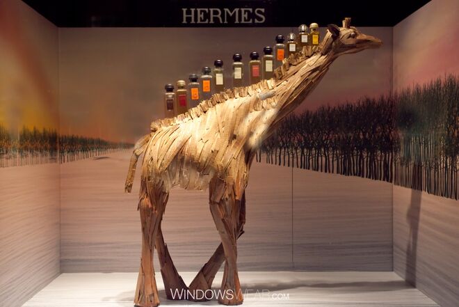 Castanho | Hermès - A gigante girafa de madeira da Hermès constitui o uso de tons ricos, quentes e terrestres. A coleção Hermès Cologne eleva-se a novas alturas com a ajuda da sua amiga de pescoço longo neste regalo para o olhar e sentidos olfativos.