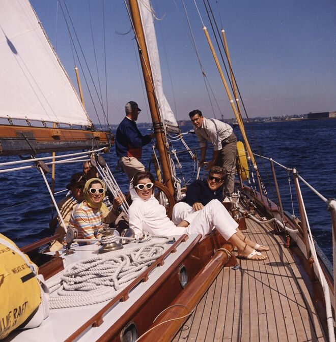 Jackie e John Kennedy na primeira corrida America’s Cup, em 1962. Jackie usa um look branco total com óculos escuros e lenço na cabeça.