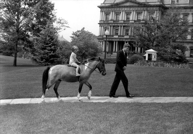 Junho, 1962 | O presidente John F. Kennedy a acompanhar a filha, Caroline Kennedy, a andar de pónei na Casa Branca, em West Wing Lawn, Washington, D.C.