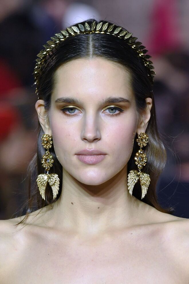 Desfile alta-costura primavera/verão 2018 Georges Hobeika: Os cabelos são levemente ondulados e divididos ao meio. A simplicidade do penteado contrasta com os acessórios, uma tiara dourada e brincos maxi.