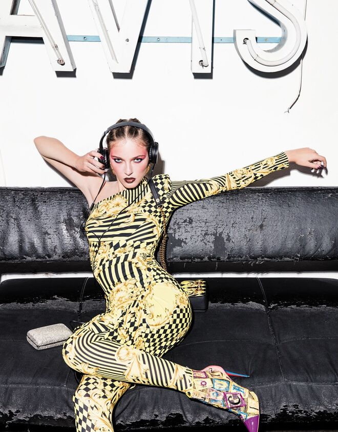 Vestido e leggings em viscose. Carteira em pele. Tudo Versace. Botins em pele e algodão, Christian Louboutin. Brincos em latão com banho de ouro, Carolina Curado. Clutch em metal e strass, Tous. Auscultadores da produção. 