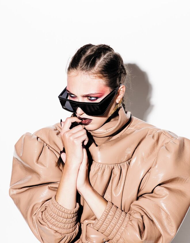 Blusão em pele envernizada, Miu Miu. Óculos em acetato com tachas metálicas, Moschino. Brincos em latão com banho de ouro, Carolina Curado.