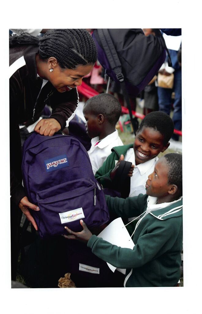 2002. Oprah Winfrey oferece mochilas a crinaçsno evento Christmas Kindness na África do Sul.