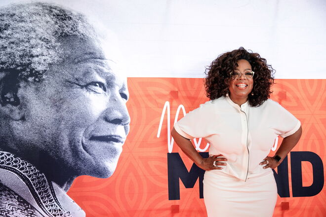 2018 | Oprah Winfrey na passadeira vermelha diante do cartaz em honra do 100º aniversário do nascimento de Nelson mandela na Universidade de Joanesburgo 