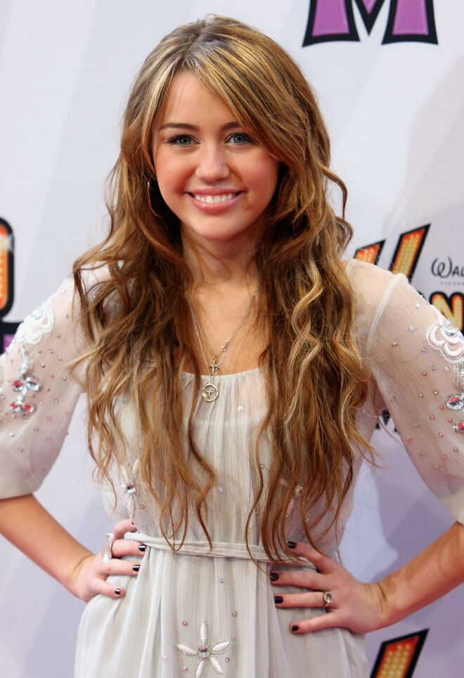 Miley Cyrus com um longo e ondulado cabelo castanho com reflexos dourados na época em que representava Hannah Montana