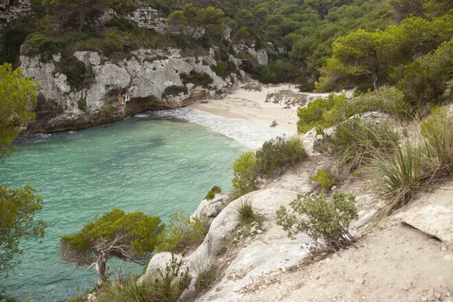 Praia Cala Macarelleta, Menorca | Situada em Menorca, a segunda maior ilha do arquipélago das Ilhas Baleares, a leste de Espanha e a oeste da Sardenha, esta praia é digna de um postal de férias. A água é tão cristalina que os iates parecem permanecer em suspenso, aqui.