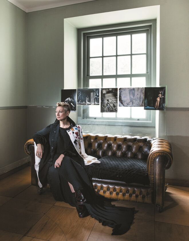 Olga Roriz no Palácio Pancas Palha, em Lisboa, a casa da Companhia Olga Roriz. A coreógrafa usa um vestido muito longo, preto e plissado sob camisa longa com punhos e colarinho em verniz, igualmente plissado, ambos Alves/Gonçalves. Casaco branco com flores bordadas com pedrarias e lantejoulas, Oscar de la Renta, na Stivali. Sapatos masculinos, Alexander McQueen.