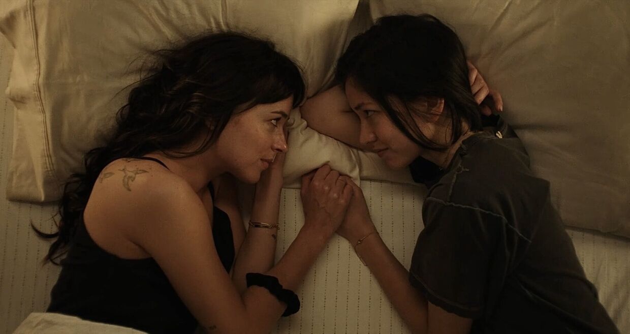 Duas mulheres de mãos dadas numa cama partilham um momento íntimo
