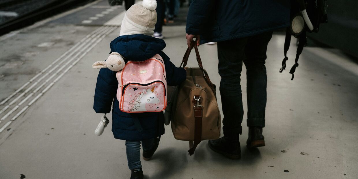 Criança e adulto caminham numa plataforma de estação de comboios com malas