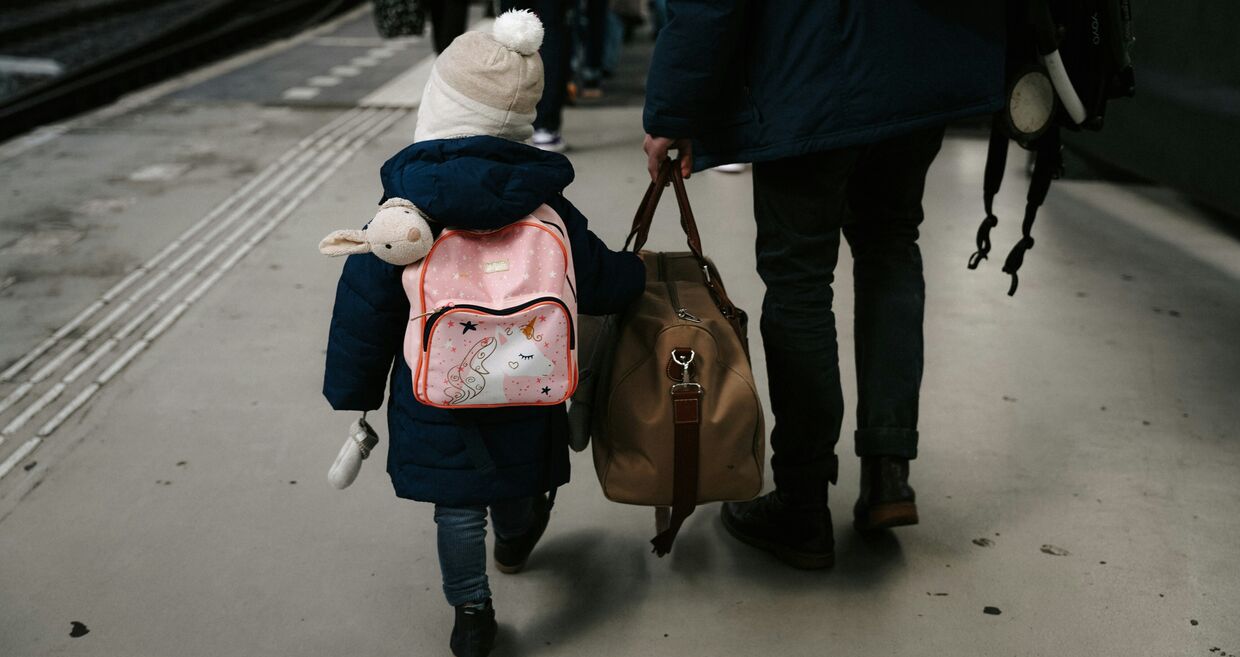 Criança e adulto caminham numa plataforma de estação de comboios com malas