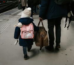 Criança e adulto caminham numa plataforma de estação de comboios com malas
