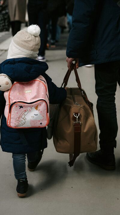 Criança e adulto caminham numa plataforma de estação de comboios com malas