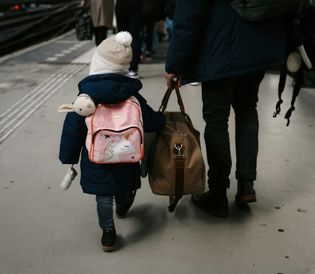 Criança e adulto caminham numa plataforma de estação de comboios com malas