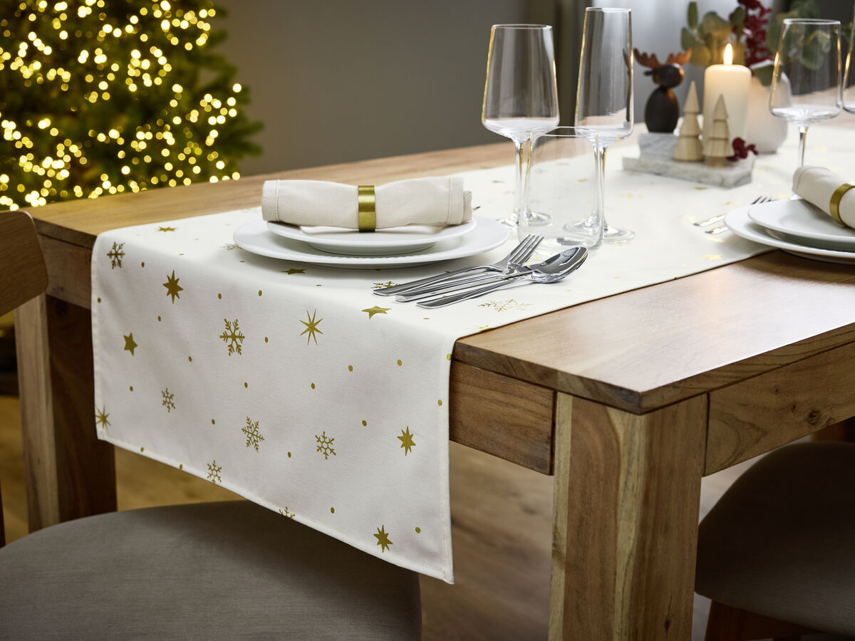 Mesa de Natal festiva com decorações e árvore iluminada ao fundo.
