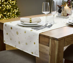 Mesa de Natal festiva com decorações e árvore iluminada ao fundo.
