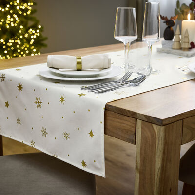 Mesa de Natal festiva com decorações e árvore iluminada ao fundo.
