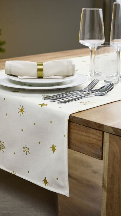 Mesa de Natal festiva com decorações e árvore iluminada ao fundo.
