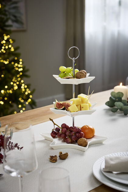 Mesa de Natal festiva com decorações e árvore iluminada ao fundo.
