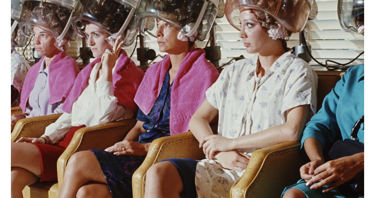 Num salão de beleza, mulheres aguardam com secadores de cabelo