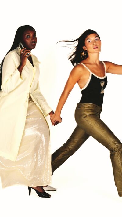 Raquel: Gabardina em nylon, Coming Soon. Saia em base de organza de seda com lantejoulas em PVC, Arndes. Sapatos, Mango. Anéis, arquivo. Colar, Coming Soon. | Concha: Fato de banho em lycra, Coming Soon. Calças em pele, Archives Explorer. Sapatos, Paulo Brandão na Coming Soon. Brincos, Beatriz Jardinha.