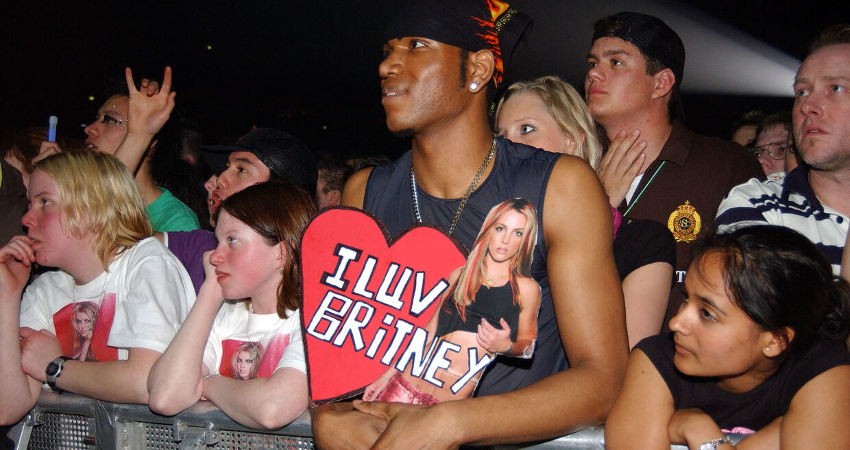 Fãs apoiam Britney Spears com cartazes e t-shirts num concerto.
