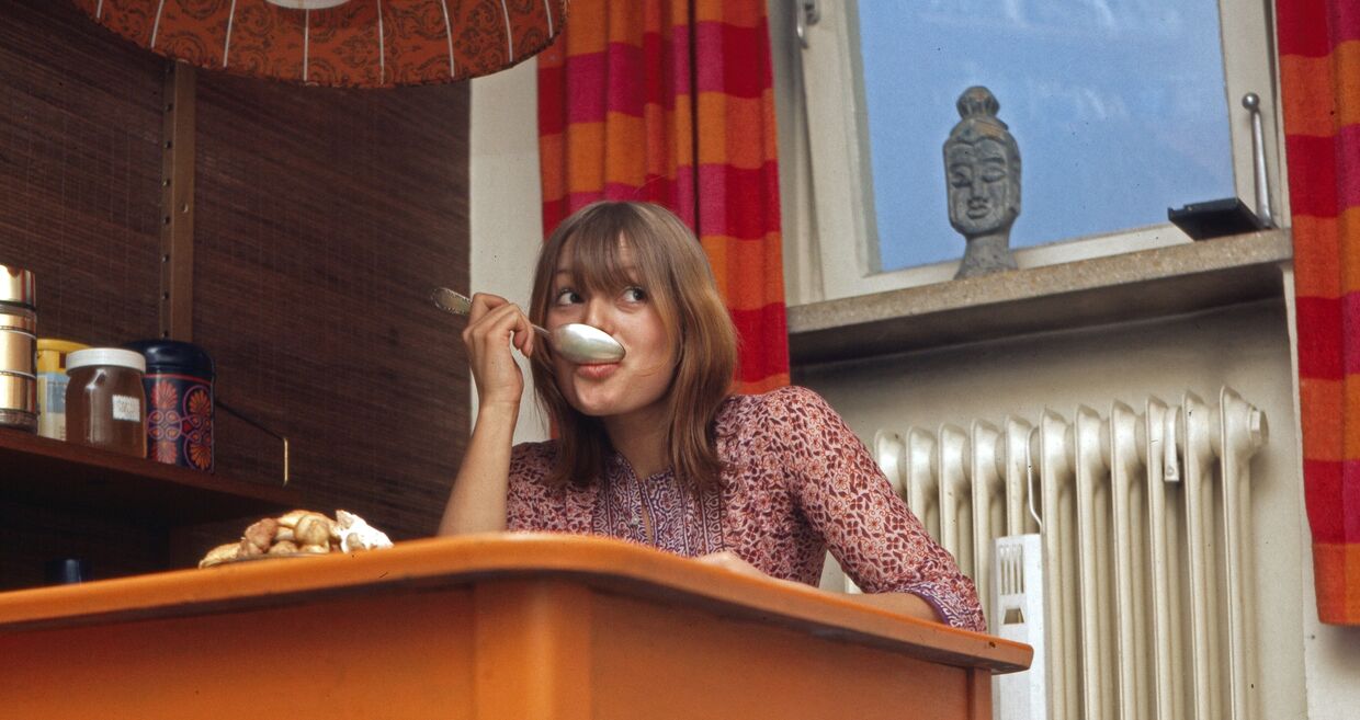 Mulher com colher na boca e mesa laranja num artigo sobre endometriose e dieta