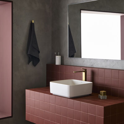 Torneira moderna destaca-se na casa de banho com azulejos vermelhos, espelho e toalha escura