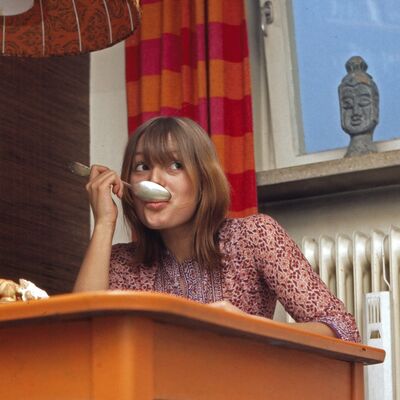 Mulher com colher na boca e mesa laranja num artigo sobre endometriose e dieta