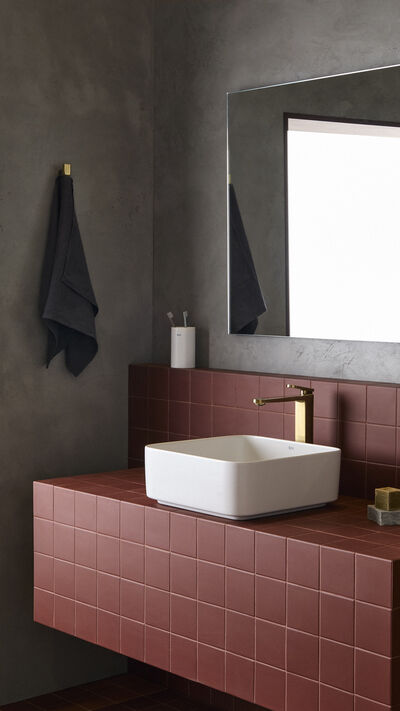 Torneira moderna destaca-se na casa de banho com azulejos vermelhos, espelho e toalha escura