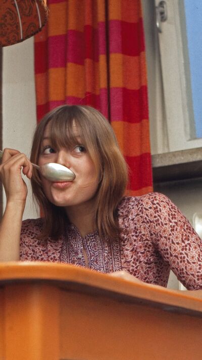 Mulher com colher na boca e mesa laranja num artigo sobre endometriose e dieta