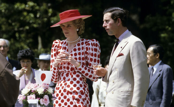 Princesa de Gales com um vestido branco de padrão polka dots em vermelho, da Tatters e completa com um chapéu vermelho de Frederick Fox. Ao seu lado está o Príncipe Carlos. 
