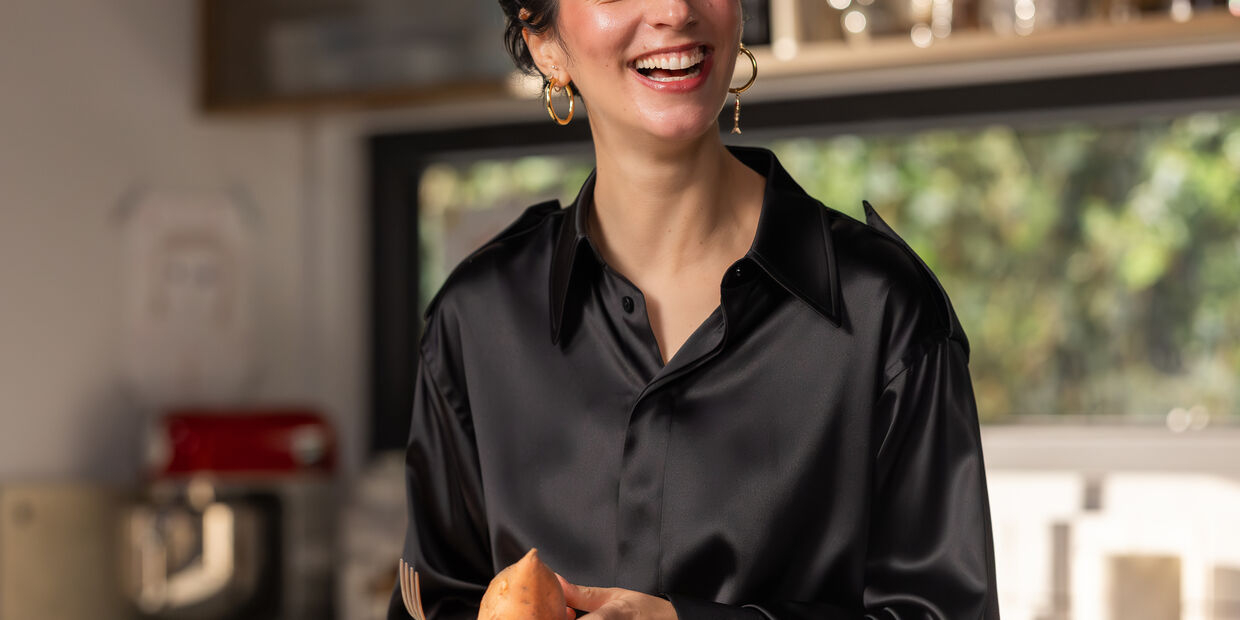 Joana Barrios prepara batata doce na cozinha, com um sorriso