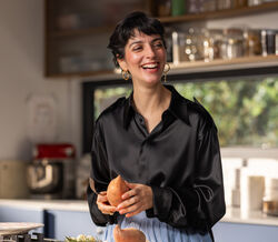 Joana Barrios prepara batata doce na cozinha, com um sorriso
