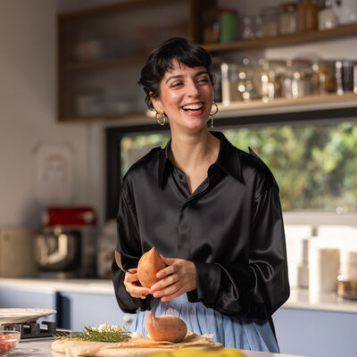 Joana Barrios prepara batata doce na cozinha, com um sorriso