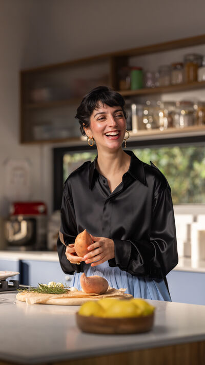 Joana Barrios prepara batata doce na cozinha, com um sorriso