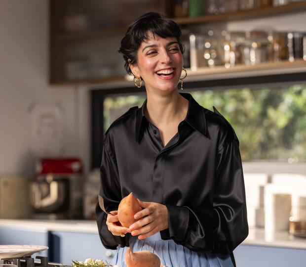 Joana Barrios prepara batata doce na cozinha, com um sorriso