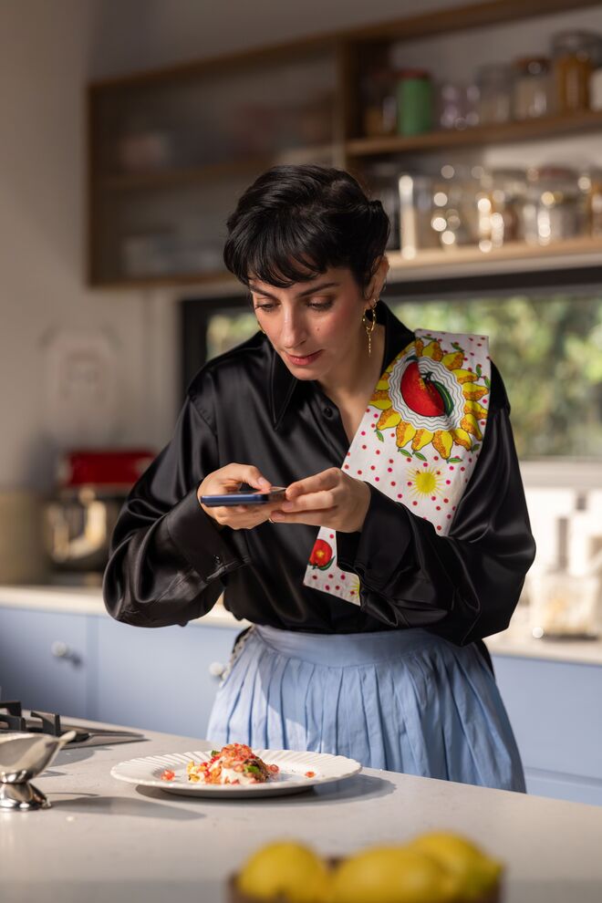 Joana Barrios prepara batata doce na cozinha, com um sorriso