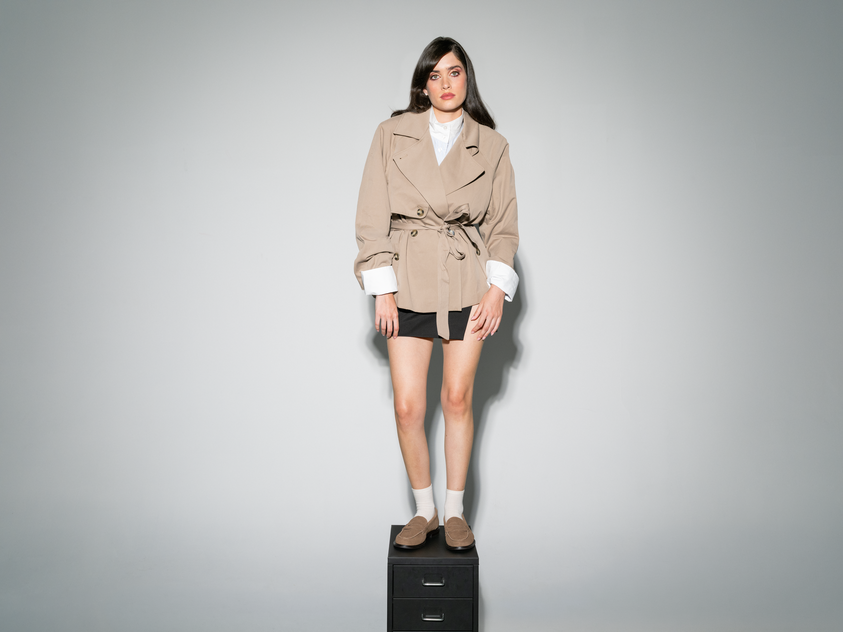Mulher com blazer e saia pousa junto a uma mesa no escritório